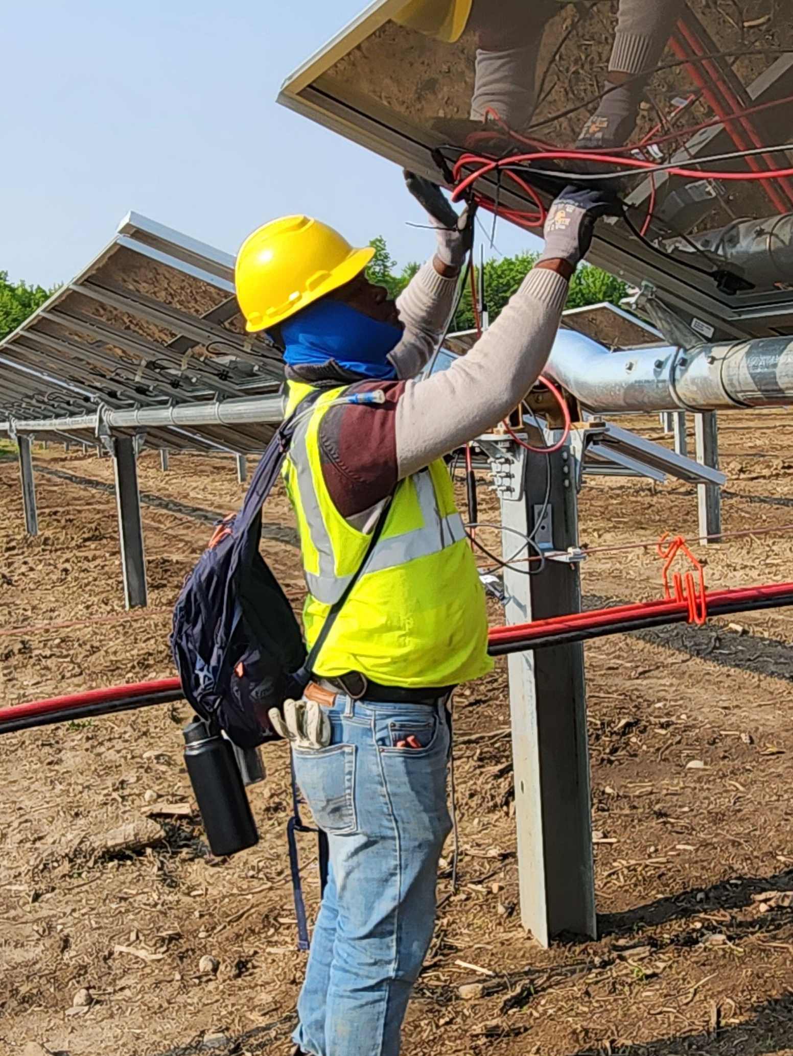 A man in yellow vest and hard hat working on solar panel.